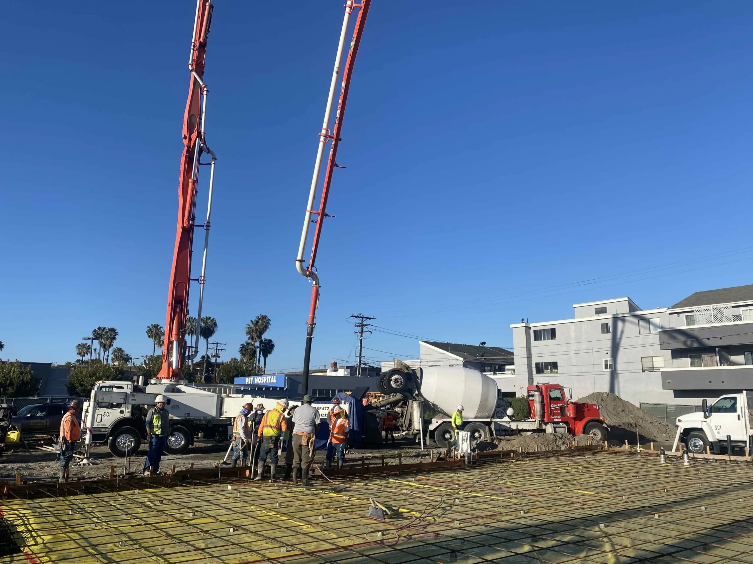 Group of people standing around a construction site with a crane, vehicles, and other objects