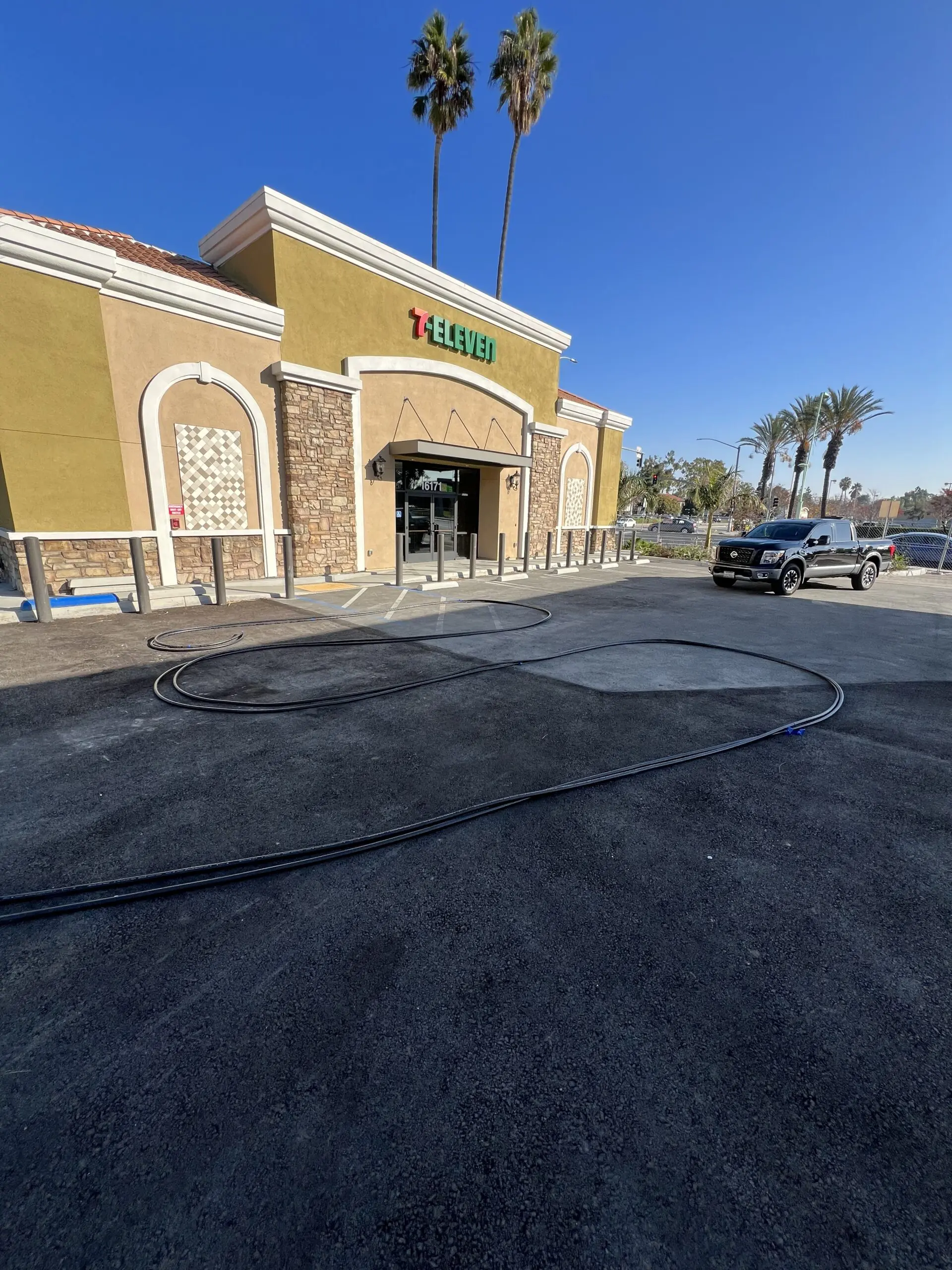 7-eleven store with a car parked in front of it, surrounded by trees, light poles, and a clear blue sky