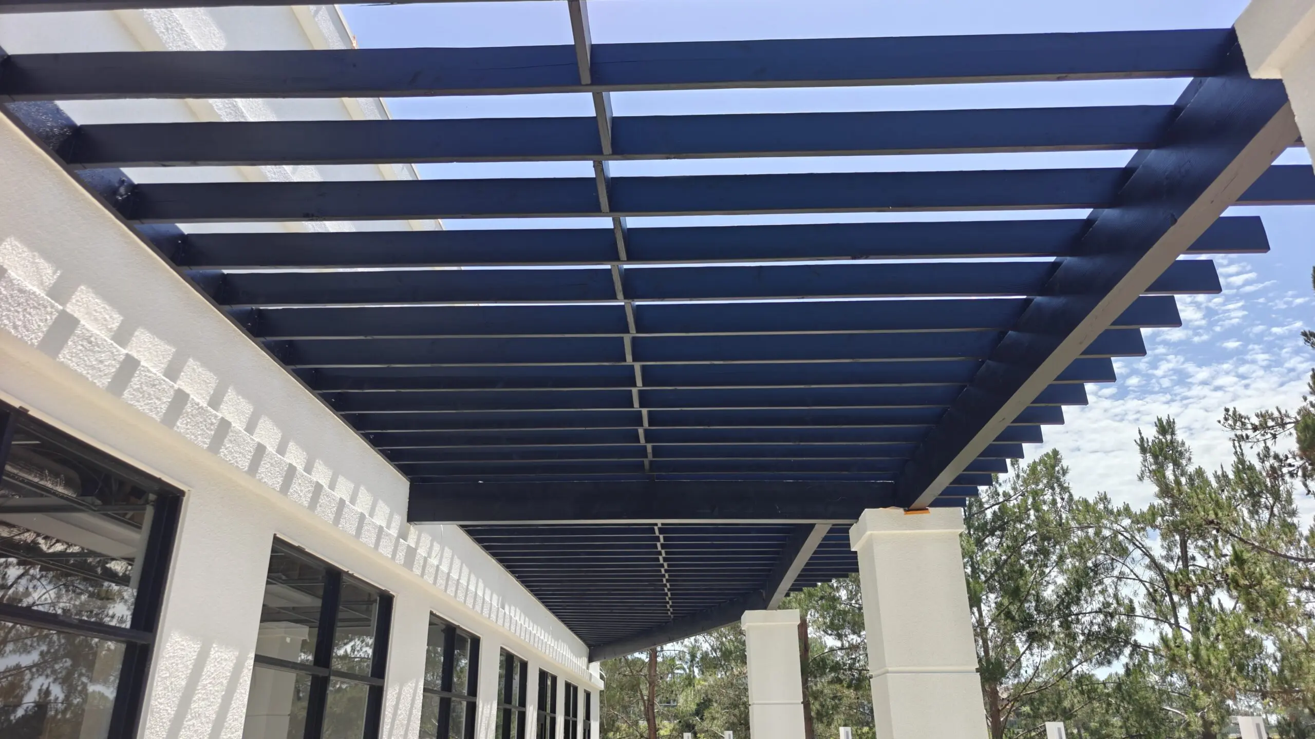 Building with glass windows and pillars, a blue pergola attached to the side of it, and trees in the background