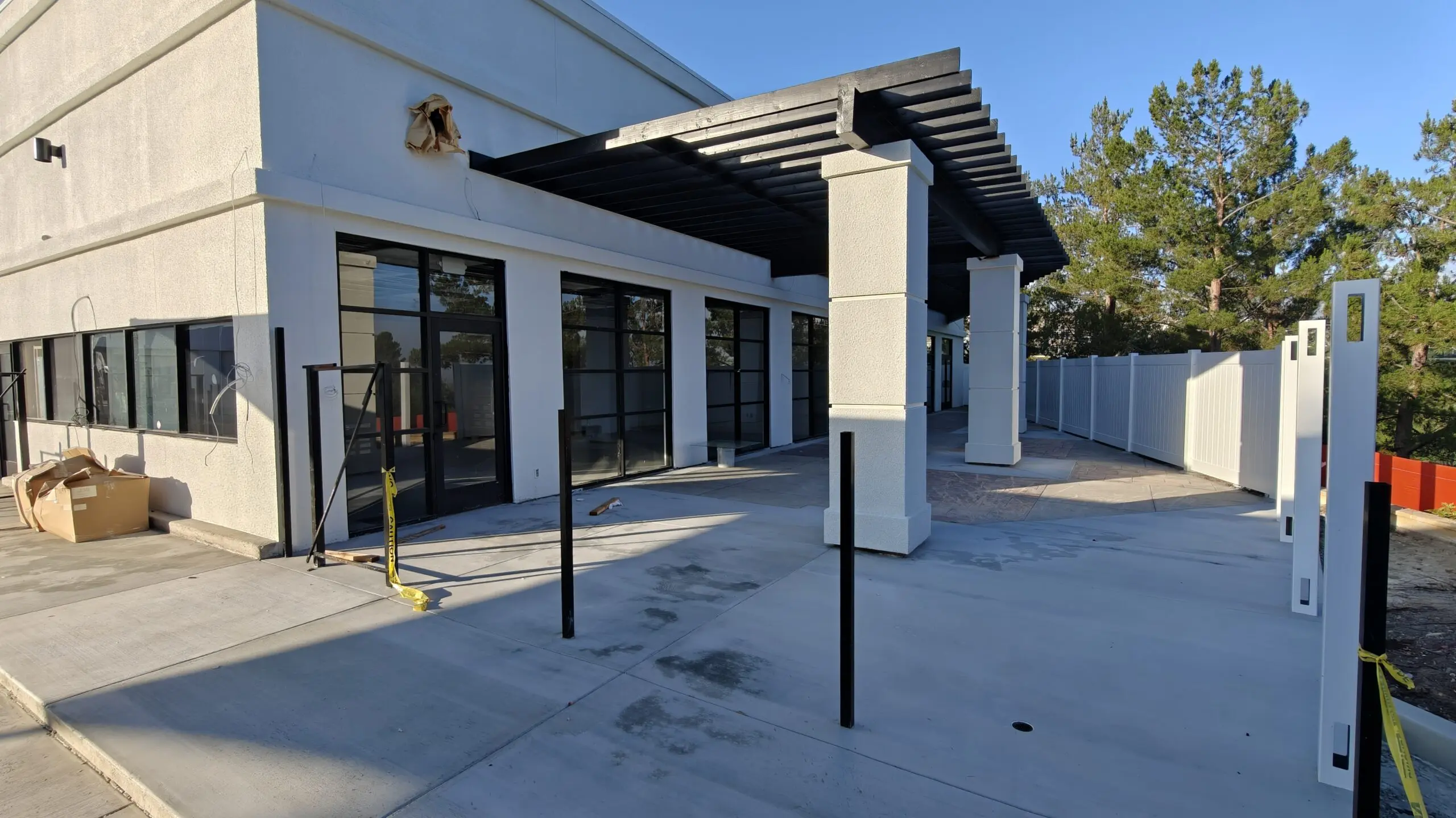 Building with glass windows and doors, a metal roof, a white fence, some poles, a cardboard box