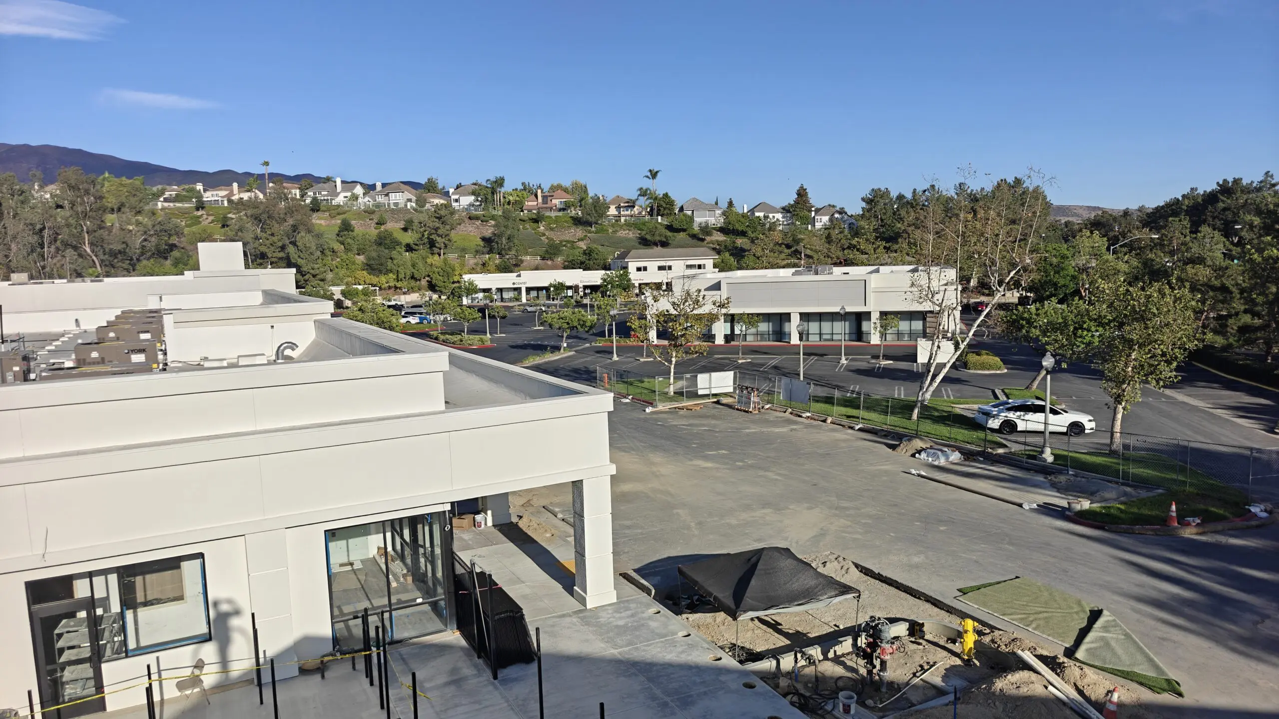 Aerial view of a building under construction in the middle of a parking lot surrounded by trees, vehicles, poles