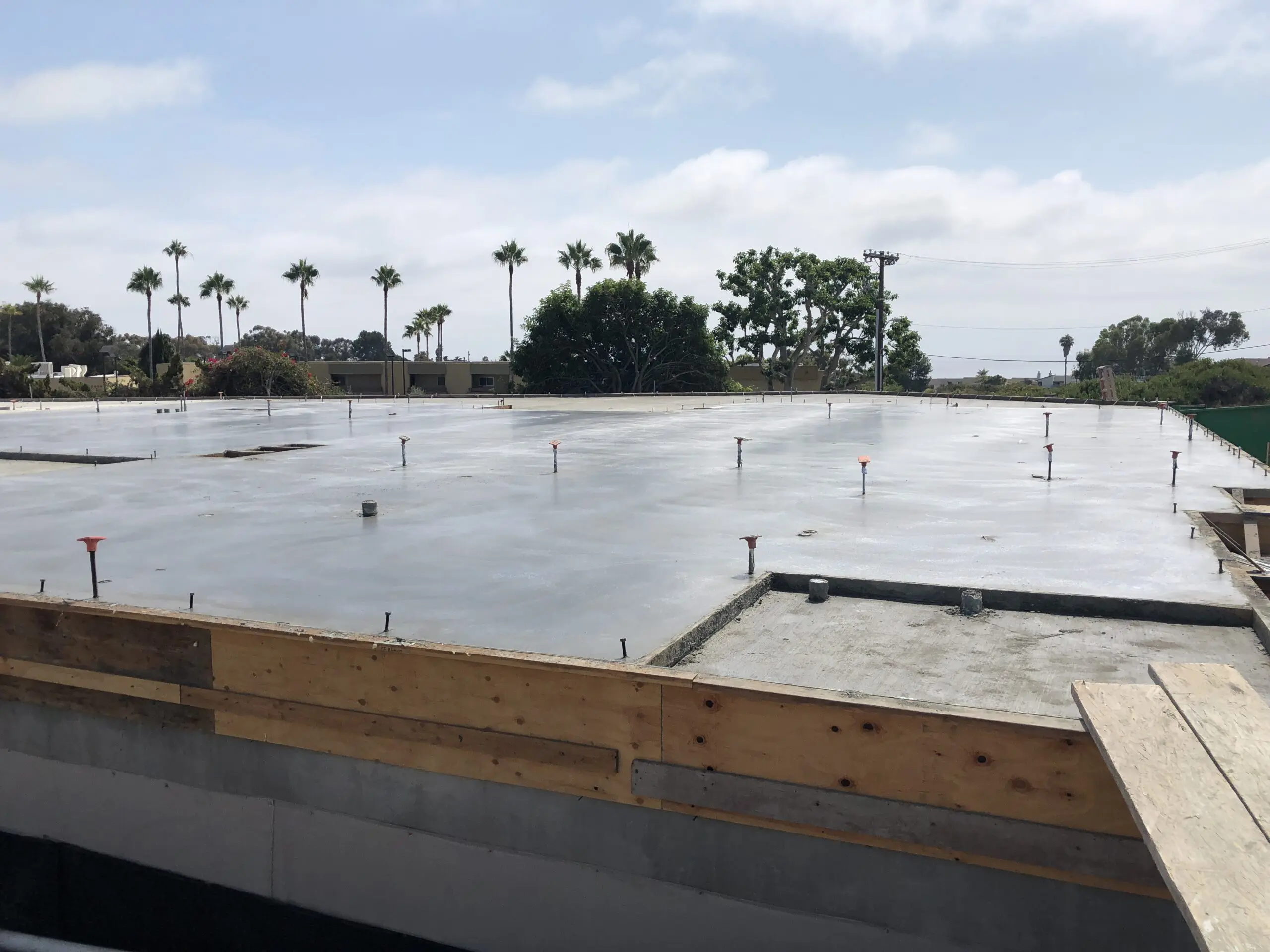 Building under construction with a flat roof and palm trees in the background