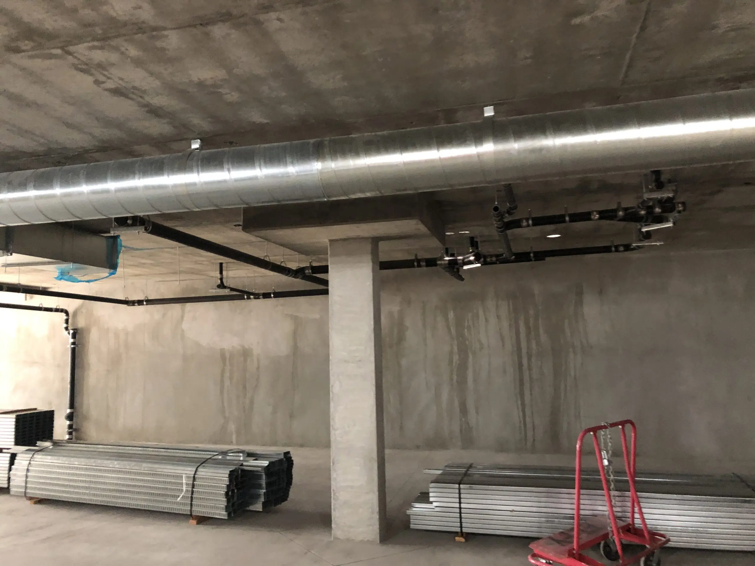 Large metal pipe in the middle of a room, surrounded by a pillar, metal sheets, a trolley