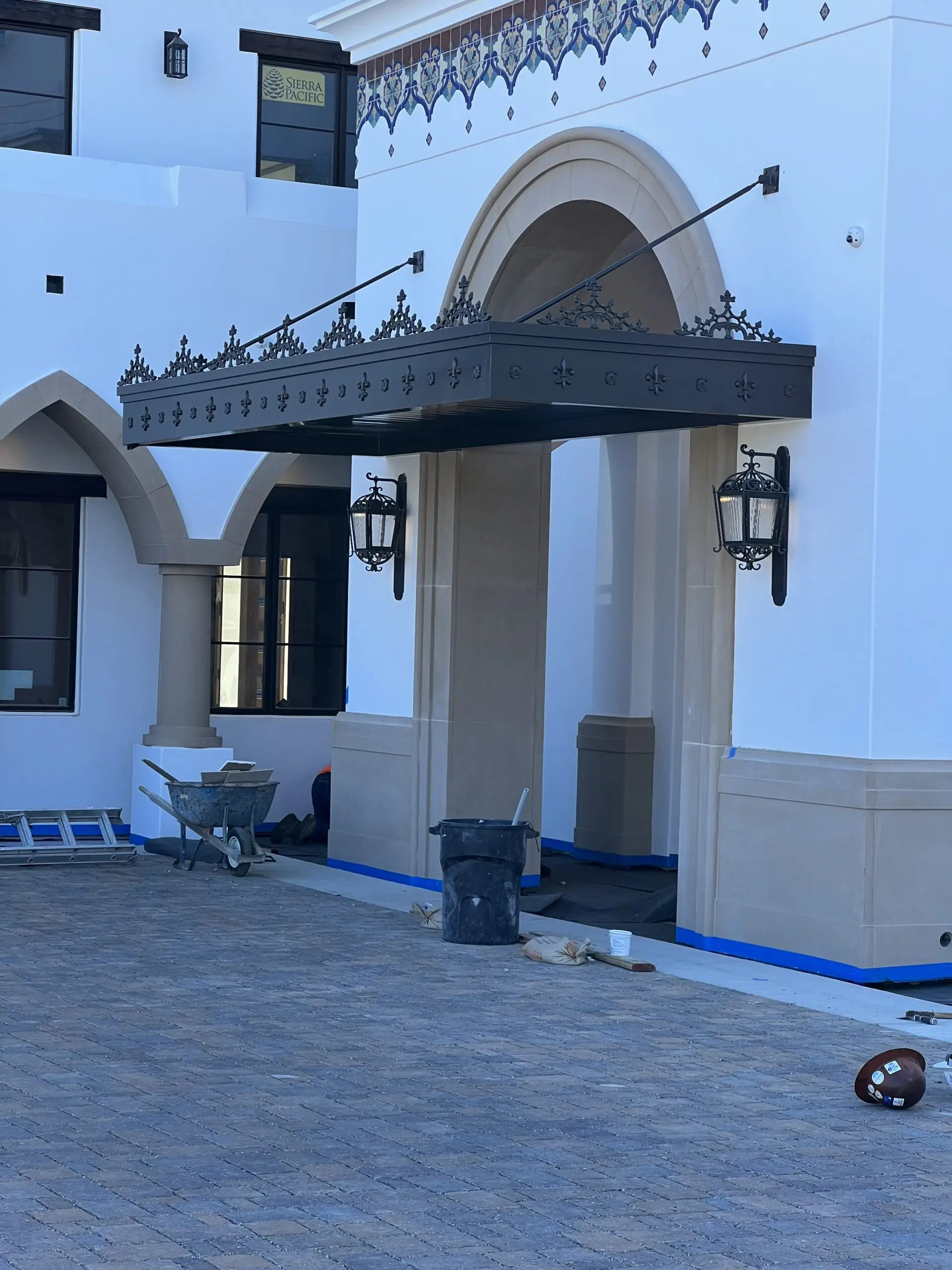 White building with a black and white awning on the side of it, surrounded by windows, lights, pillars, a trolley