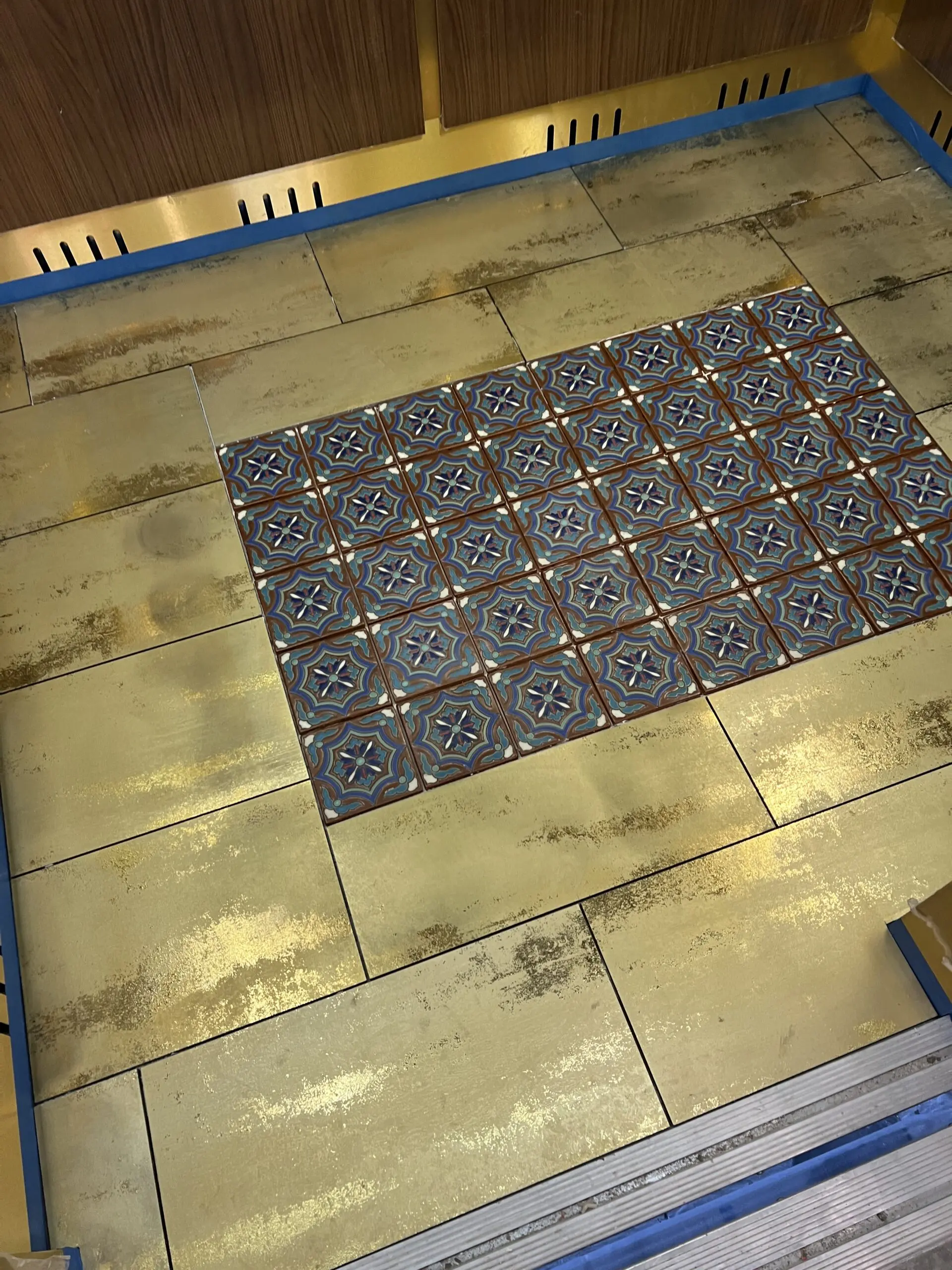Kitchen floor with a blue and gold tile on it, and a wooden wall in the background