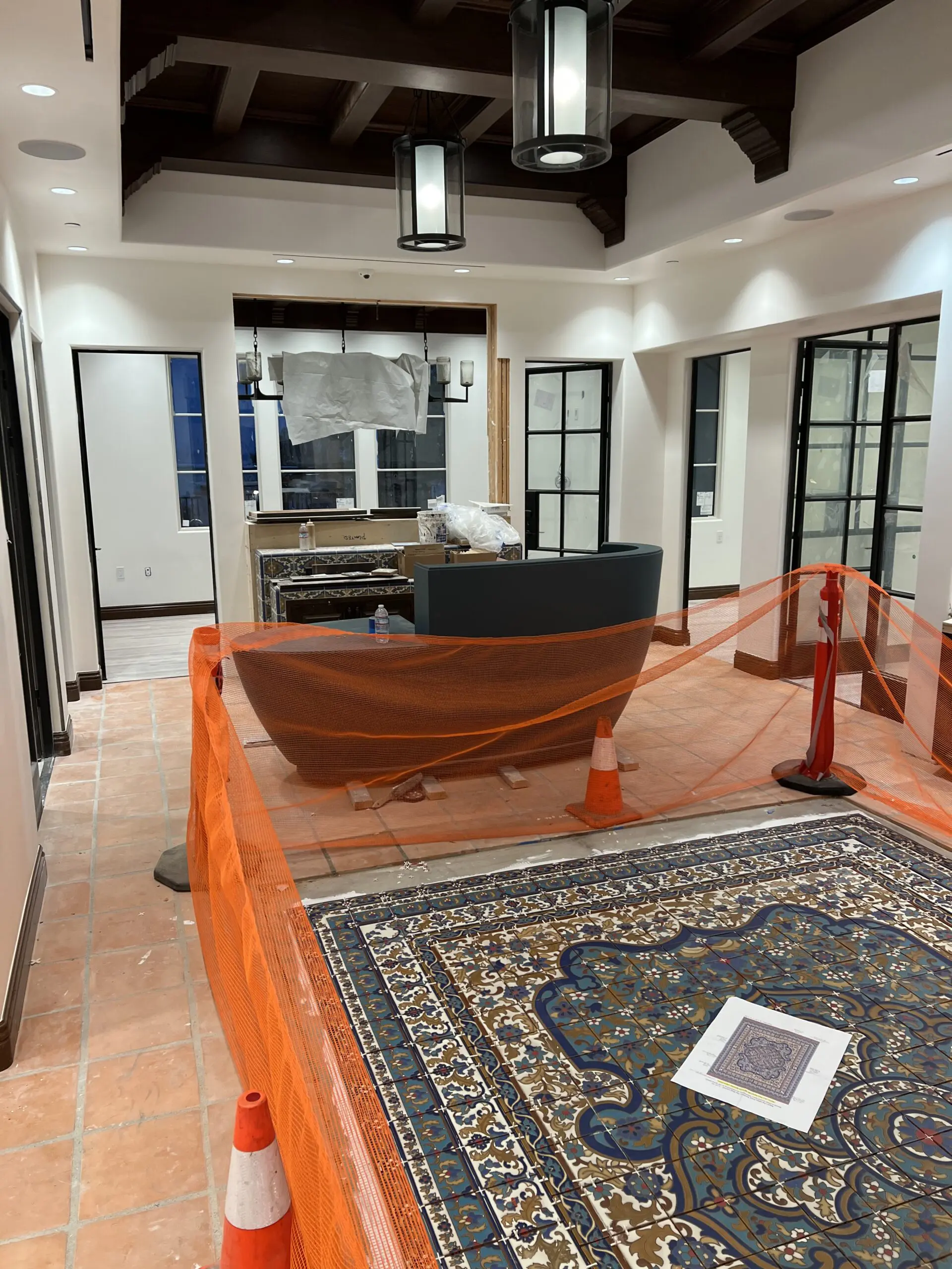 Large room with a carpeted floor, orange traffic cones, a paper on the carpet, a net, a sofa, a table