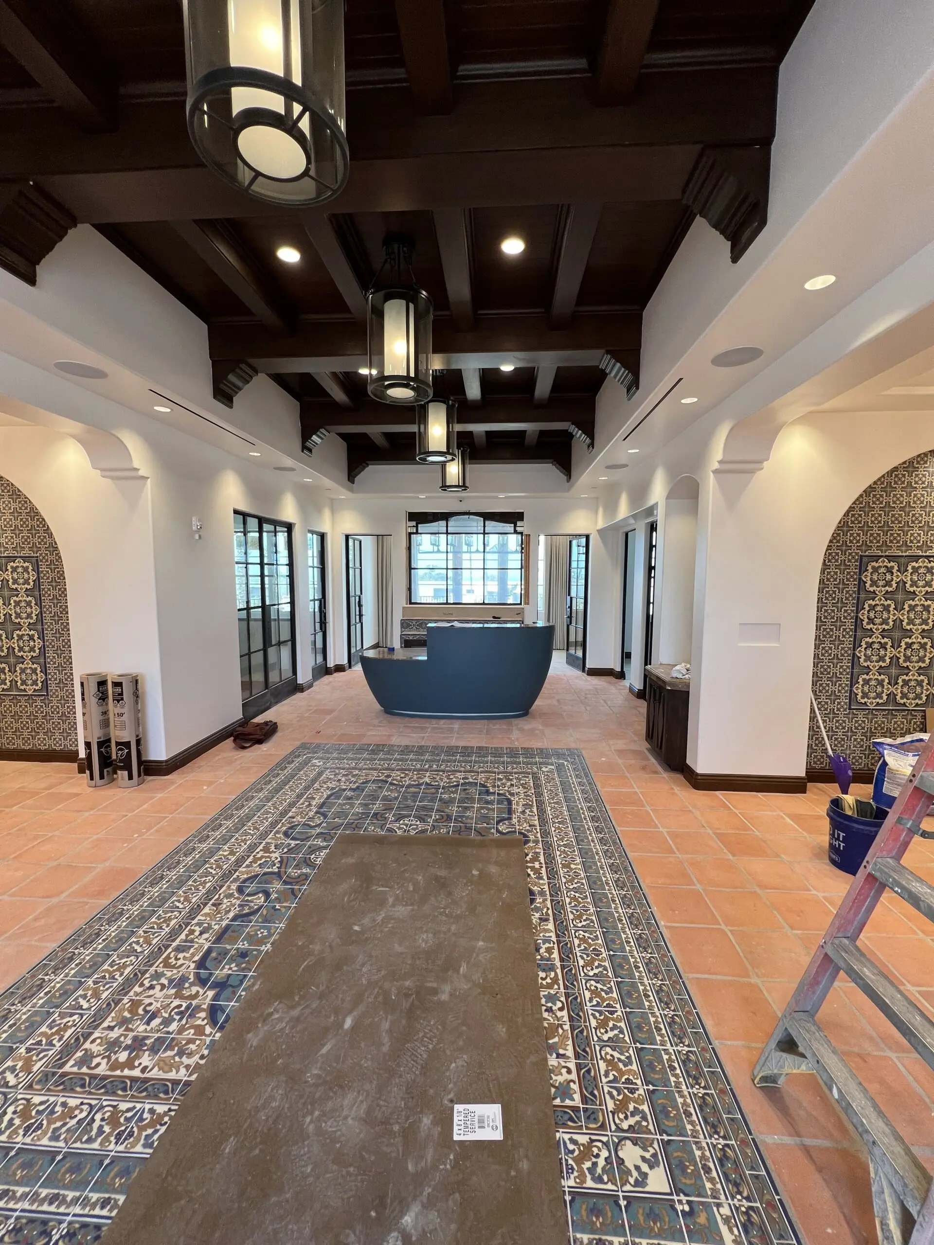 Large lobby with a large rug on the floor, a desk, a ladder, a bucket, and various objects scattered