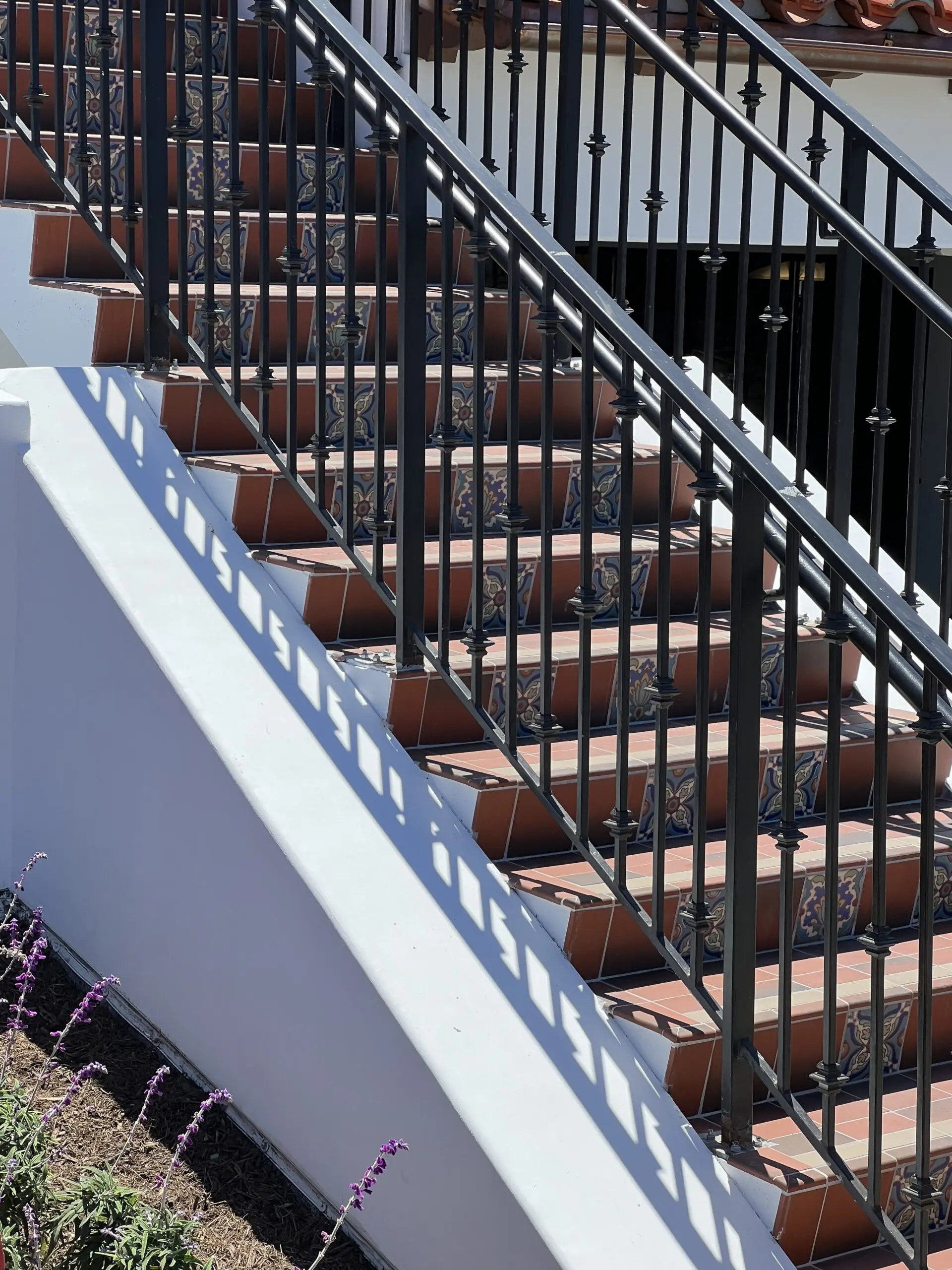 Set of stairs with a black railing and purple flowers in front of a building