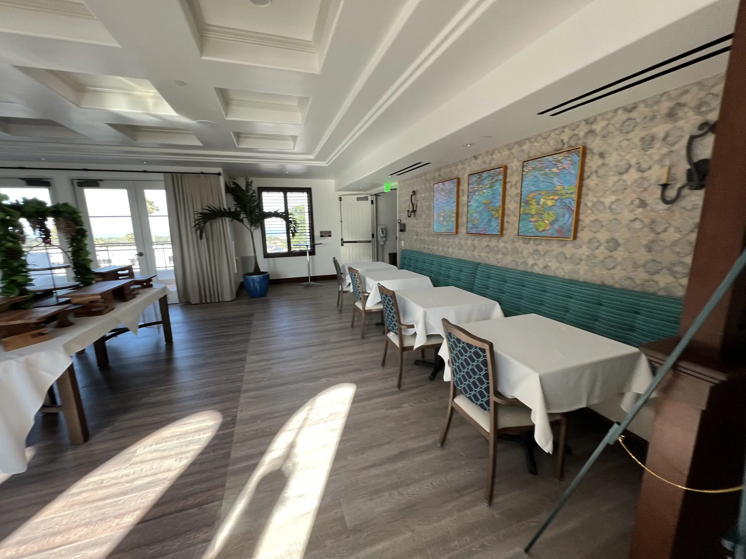 Restaurant with tables and chairs arranged in it, a desk, a houseplant, frames on the wall, lights, a door, curtains