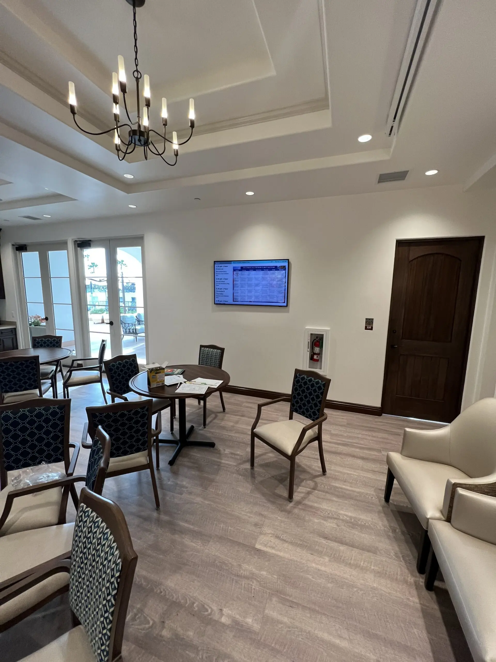 Waiting room with chairs and tables arranged around a desk, a sofa, a door, a television mounted on the wall