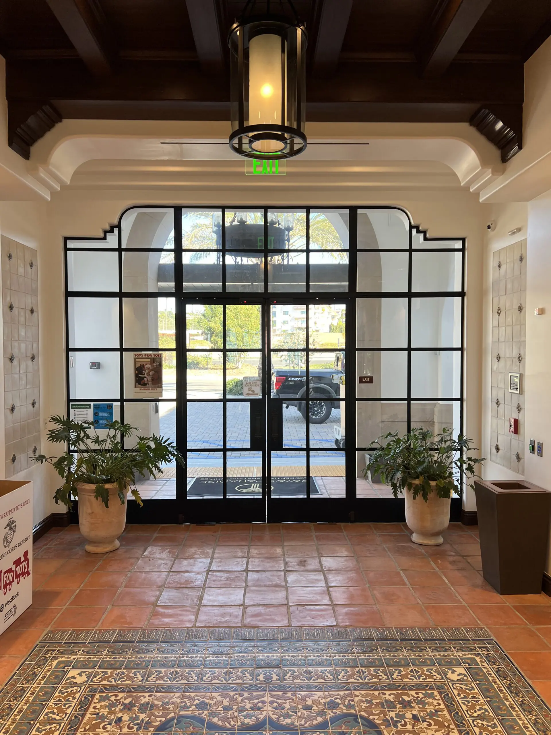 Entrance to a building with a large glass door, a carpeted floor, houseplants, a board with text printed on it