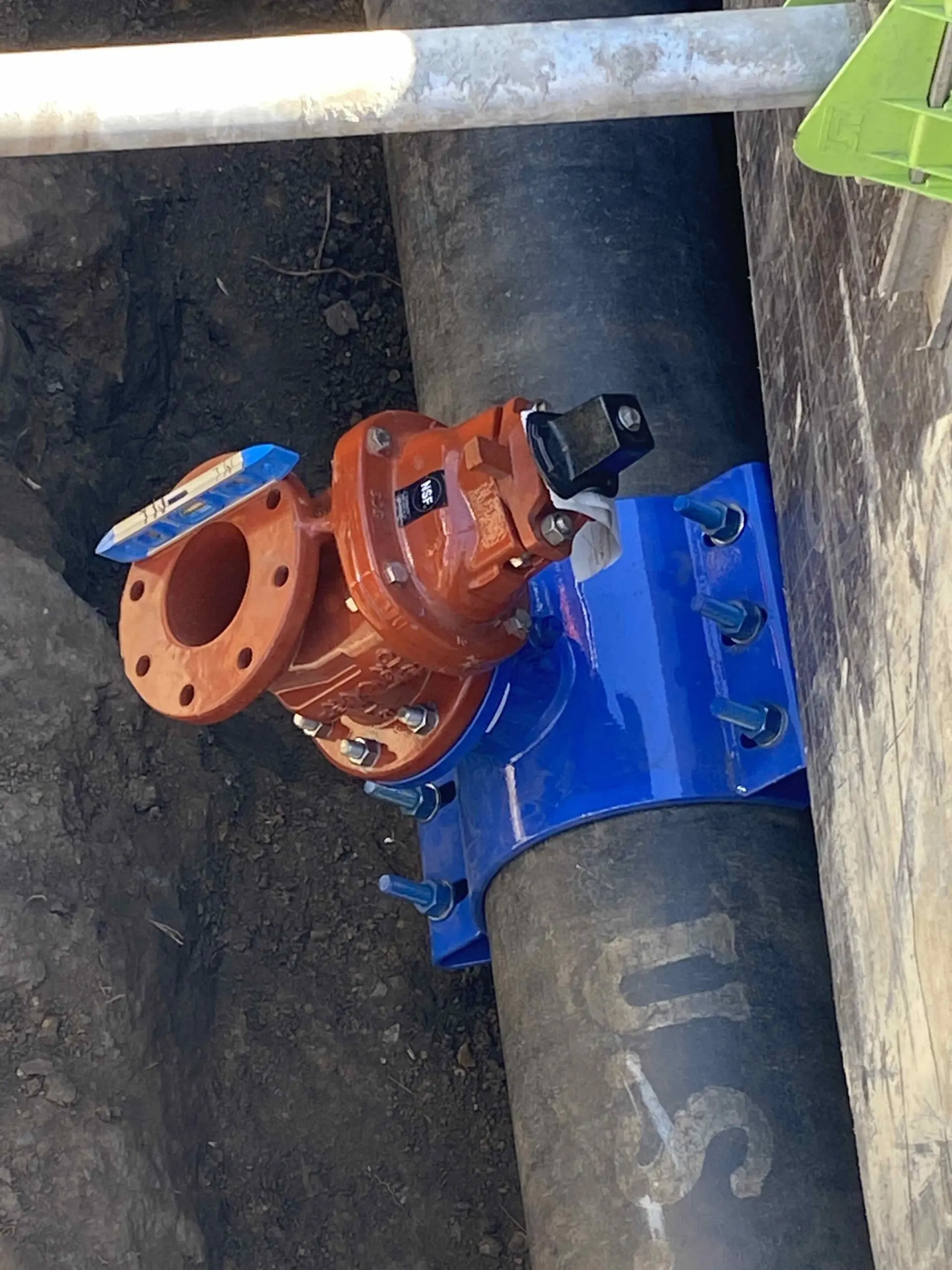 Blue and orange pipe with a green object on top of it, sitting in the dirt
