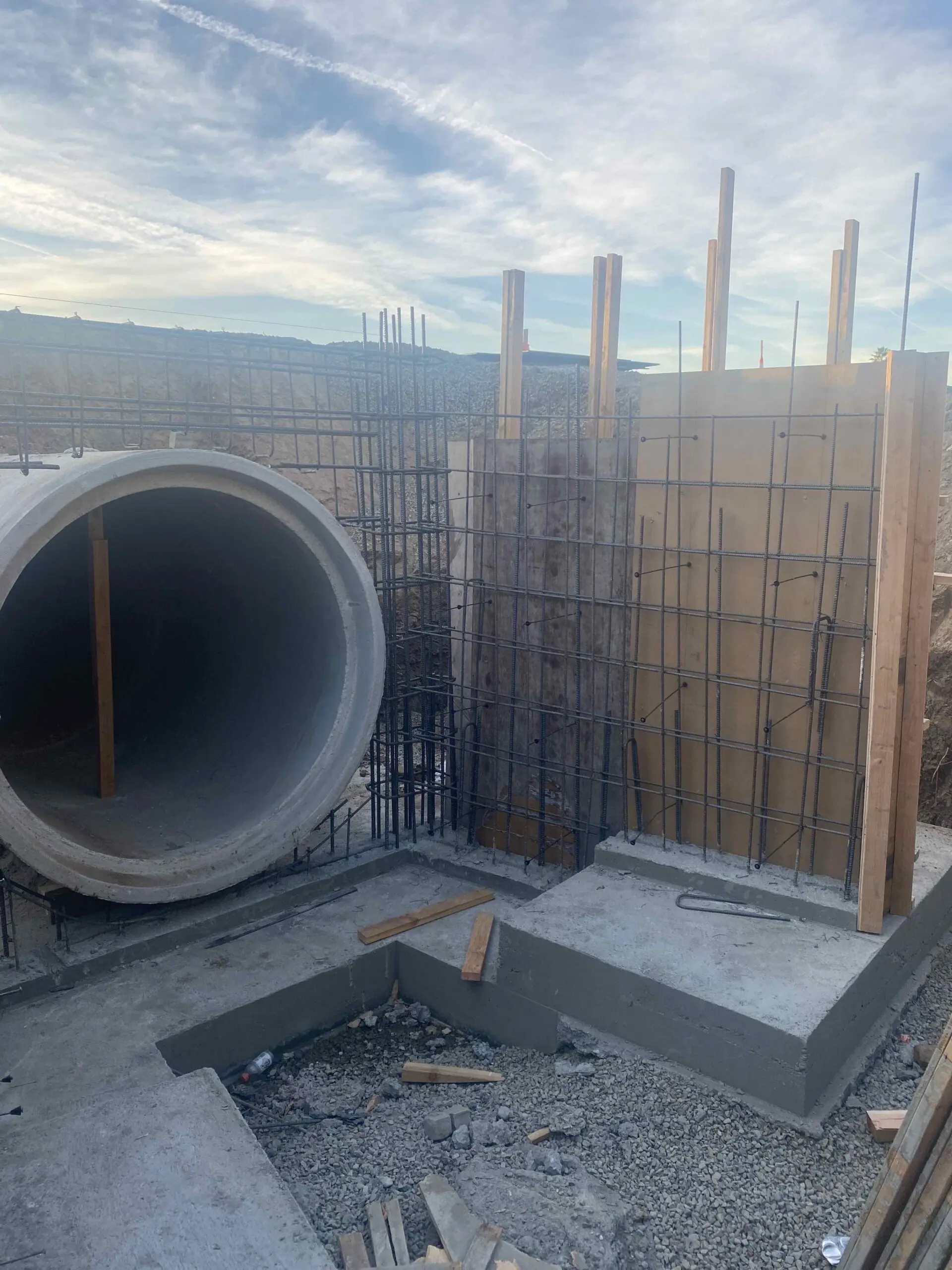 Construction site with a large concrete pipe in the middle of it, surrounded by iron rods and wooden sticks