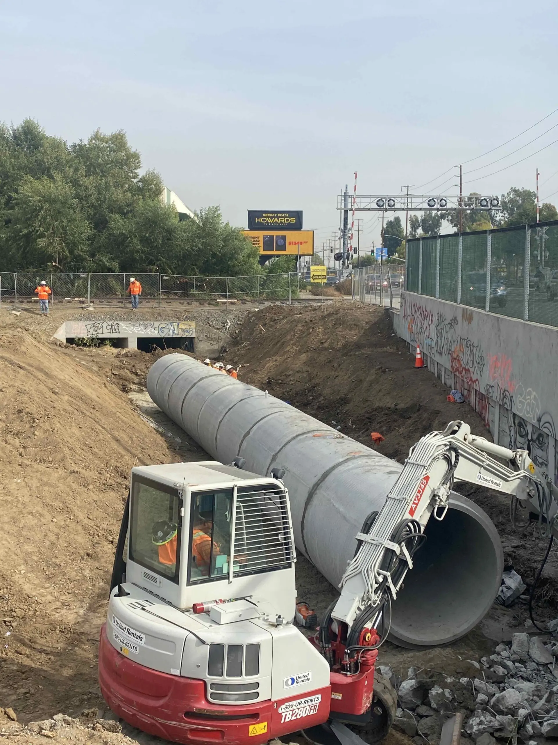 Construction site with a large pipe in the middle of it, surrounded by a fence, traffic cones, stones