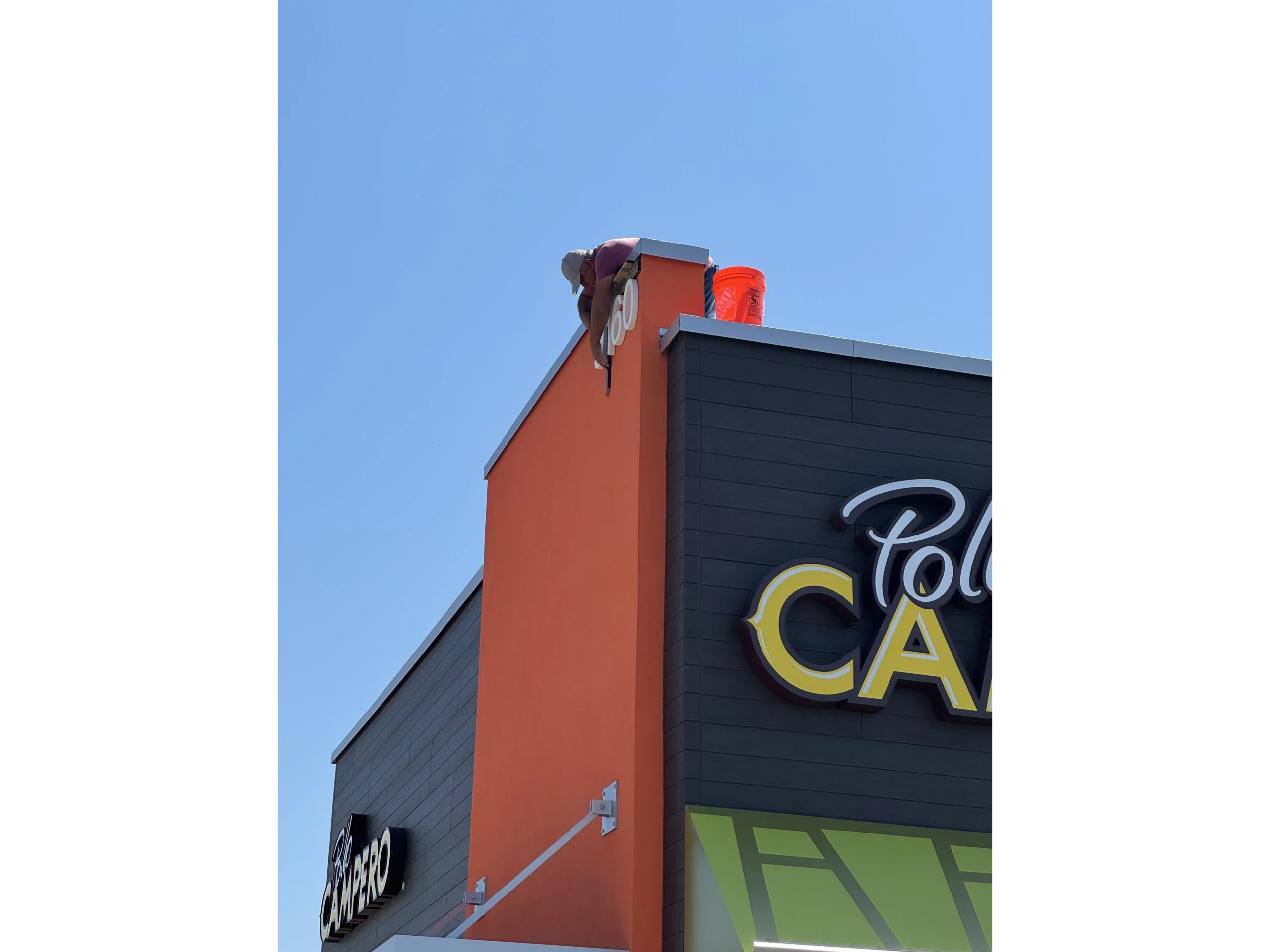 Man standing on top of a building with a sign that reads "" and a bucket of paint on the side