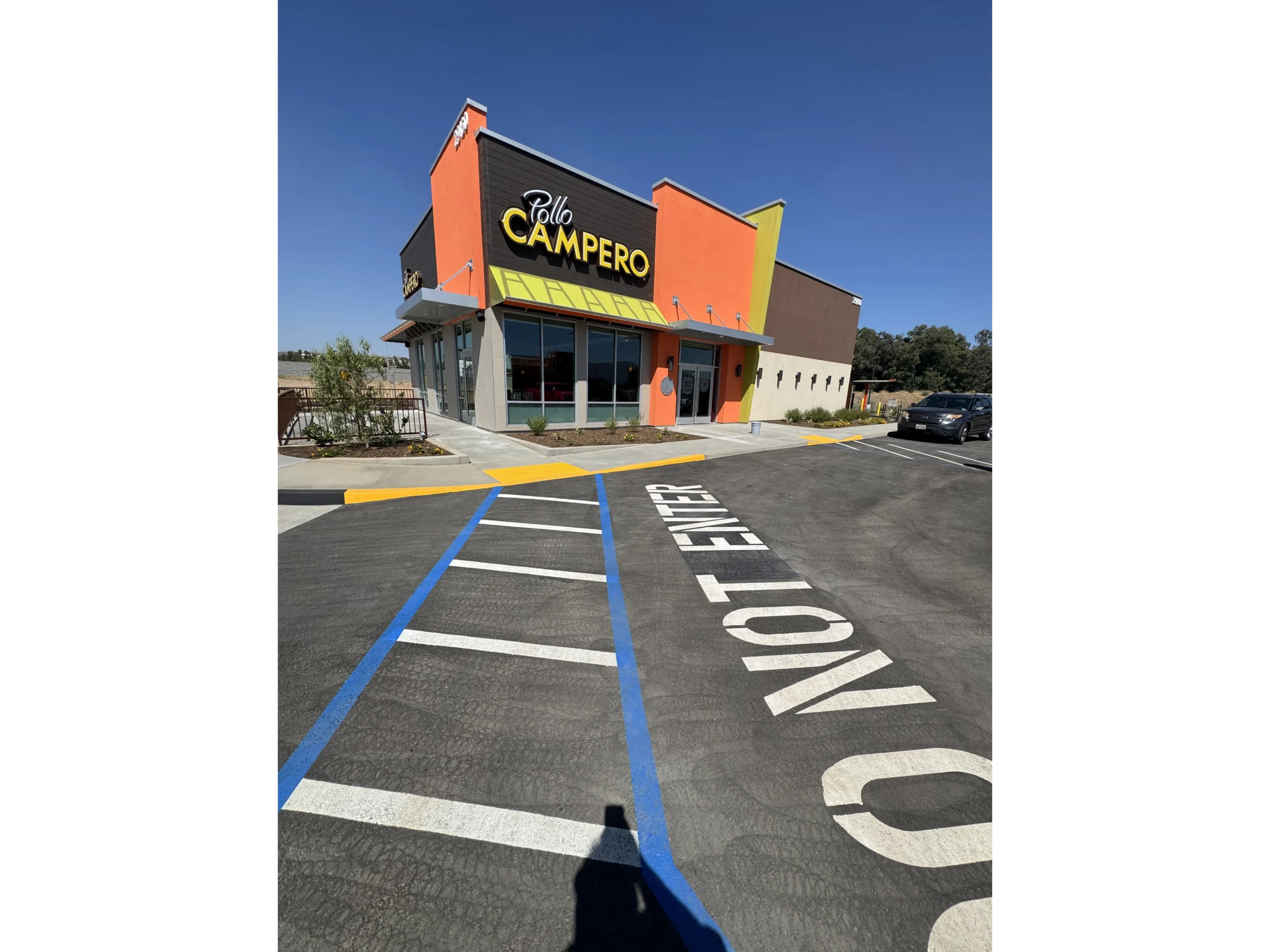 Building with a sign that reads "Pollo Campero" in front of it, surrounded by plants, trees