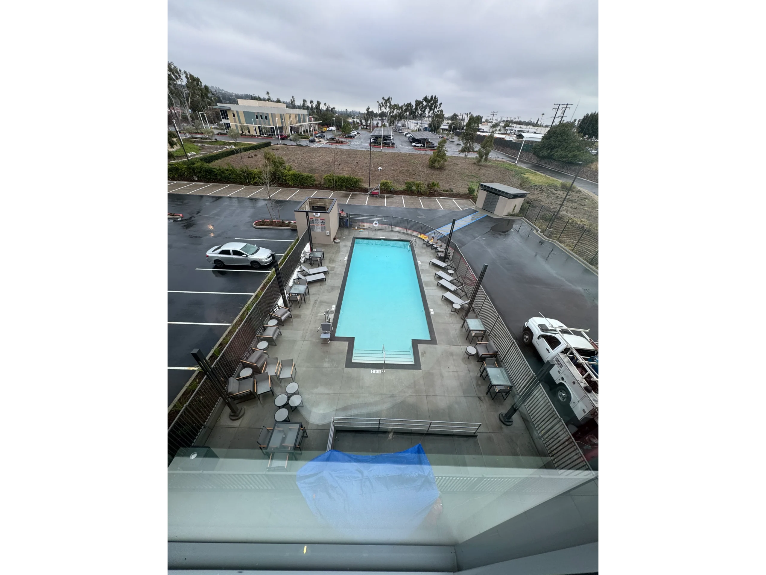 Swimming pool from the top of a building, surrounded by tables, chairs, and a fence