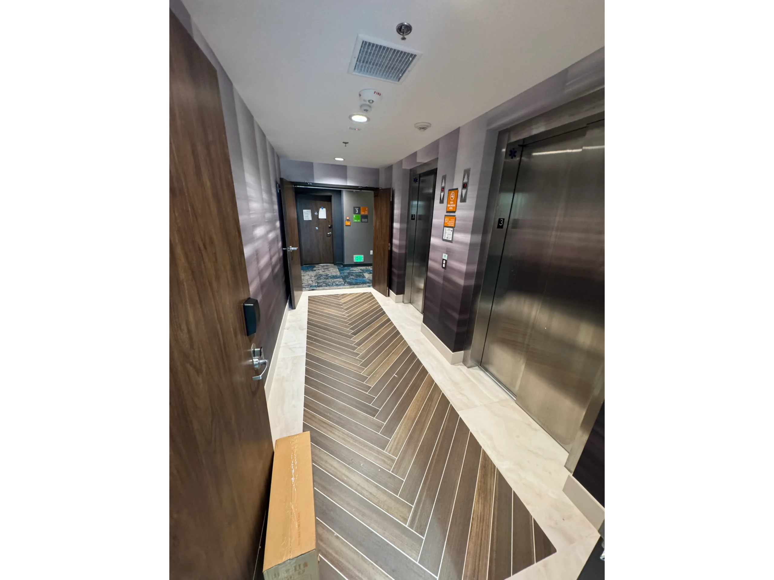 Long hallway with two elevators and a wooden door