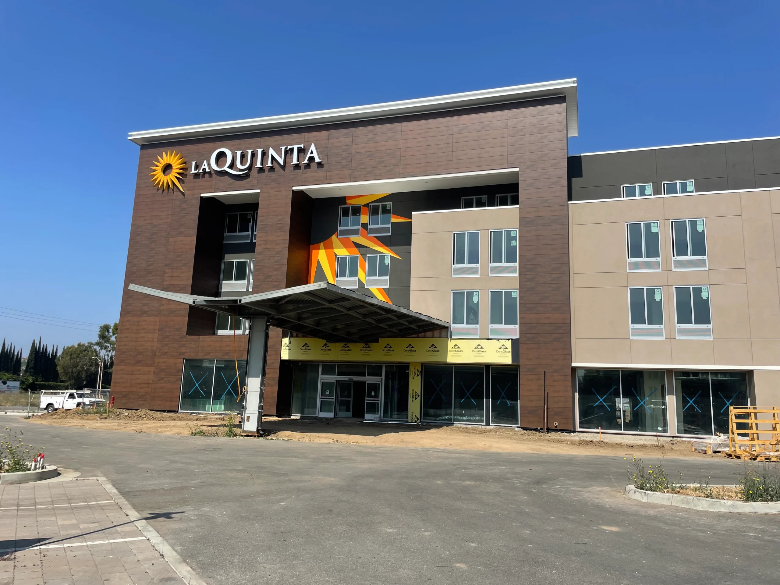 Building with windows and a sign that reads "La Quinta" in front of it, surrounded by plants with flowers